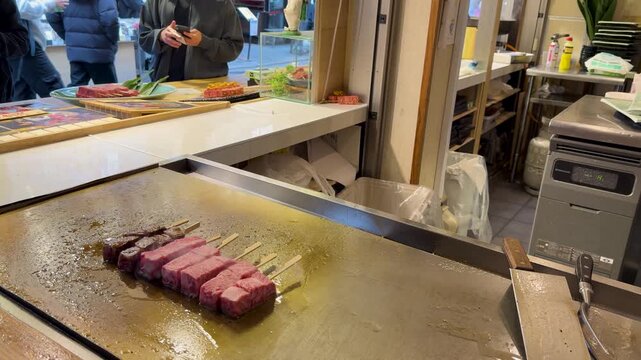 Fresh wagyu beef skewers sizzling on hot flat grill at japanese street food market.