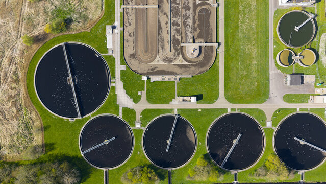 Aerial view of the RWZI Geestmerambacht wastewater treatment plant featuring circular sedimentation tanks and rectangular basins surrounded by green lawns Warmenhuizen, Noord-Holland, Netherlands.