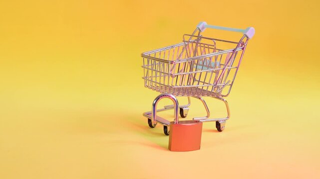 A small shopping cart stands next to a padlock with a flashing light. The cart symbolizes commerce, the padlock suggests security or restriction.