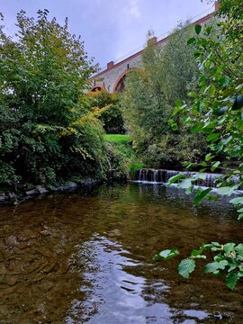 Stone viaduct bridge over forest stream with small waterfall