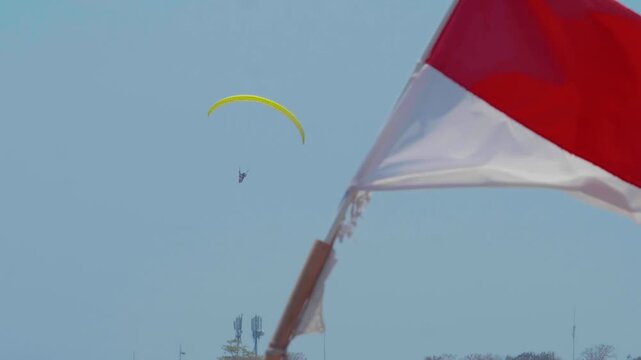 Indonesian flag flies as paraglider flies around in the background