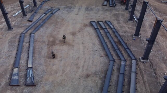 Workers on Metal frame construction site carry pipe tilt drone aerial cloudy