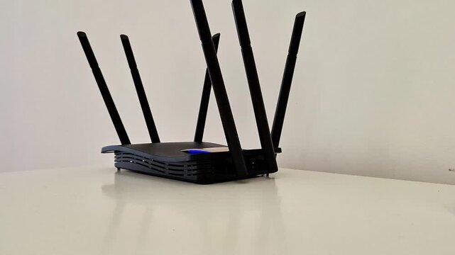 Black wired router with six antennas and glowing blue indicator light on white surface, highlighting modern connectivity, strong signal strength, and reliable network performance