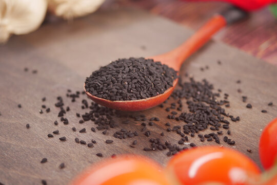 Black cumin seeds on wooden spoon with red tomatoes nearby
