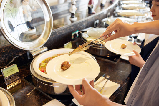 Guests taking food from a hotel buffet line with serving tongs