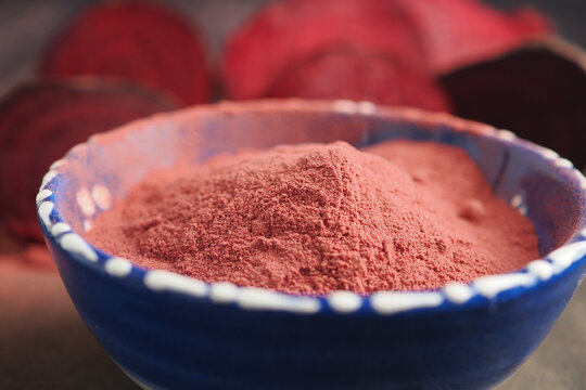 beetroot powder sits in a blue bowl with beets behind it