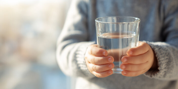 Close up of young child hands holding glass of clear water, showcasing innocence and purity in bright setting