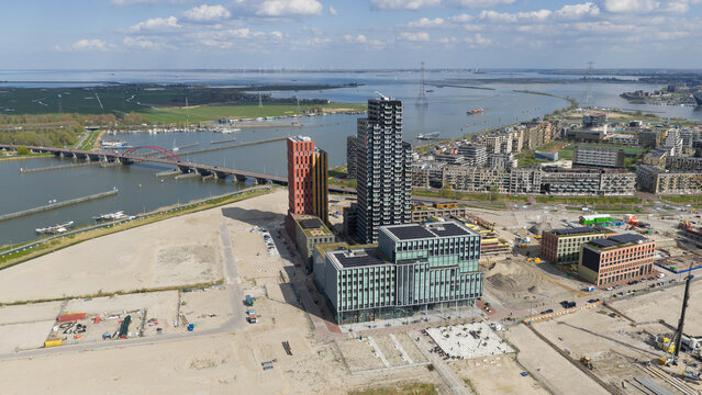 Aerial view of the modern Sluisbuurt district with high-rise residential towers, construction sites, and the Enneus Heerma Bridge over the IJ river in Amsterdam, North Holland, Netherlands.