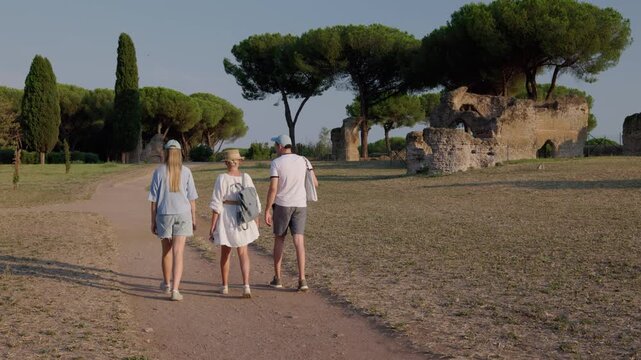 Family walking along path in Appia Antica Park Rome with ancient ruins and pine trees in warm evening light