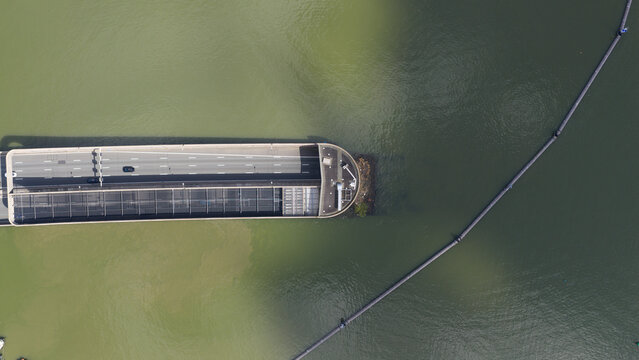Aerial view of the Zeeburgertunnel entrance with a car on the highway and a floating barrier in the green water in Amsterdam, Noord-Holland, Netherlands.