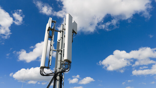 Aerial view of a telecommunications mast with white panel antennas and black cables against a blue sky with white clouds at Zuider IJdijk Amsterdam, Noord-Holland, Netherlands.