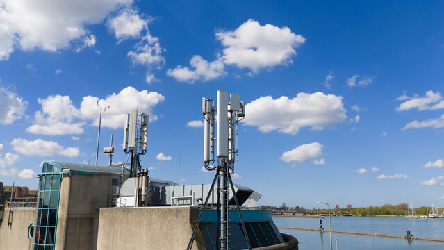 Aerial view of telecommunication antennas and 5G towers on a modern building at Zuider IJdijk overlooking the water under a bright blue sky with clouds in Amsterdam, Noord-Holland, Netherlands.