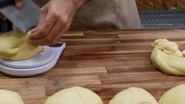 Male baker portioning raw dough on digital kitchen scale in the bakery