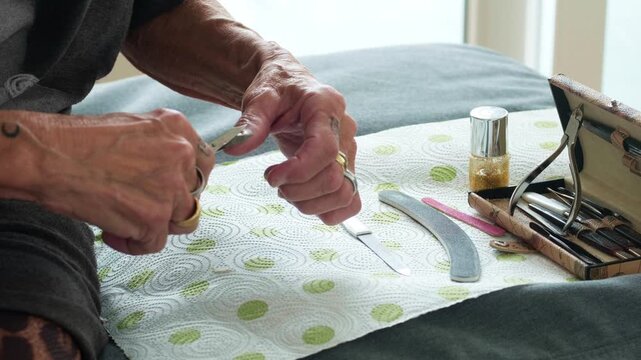 Detail shot of a woman filing her nails on a soft surface. Clean and bright aesthetic focusing on hand grooming and personal beauty care for lifestyle and wellness commercial use