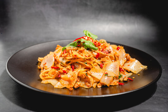 Basil wide rice noodles with minced chicken in a black plate.