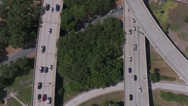 Top-down aerial view of the complex overpass exchange of Interstate highways and on ramps during rush hour with busy vehicle traffic and a constricted tree in the center.
