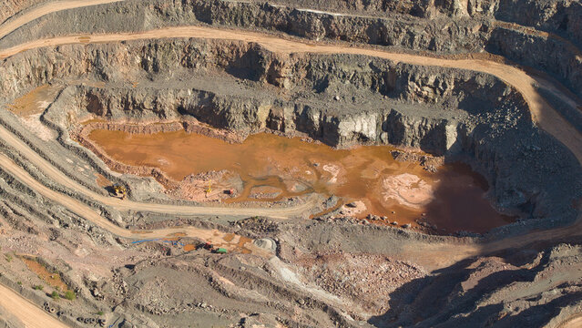 Aerial view of Old Cliffe Hill quarry showing terraced rock faces, a muddy pool of water, and heavy machinery on dirt tracks in Stanton under Bardon, England, United Kingdom.
