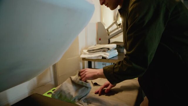 Tilt up medium closeup shot of man folding garments on worktable in printing studio, showing final step of apparel production and order preparation