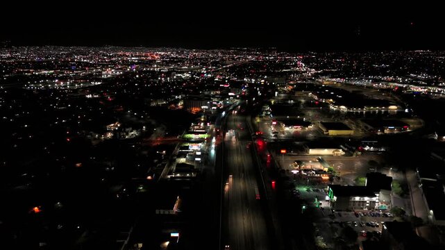 Aerial night view of urban highway with moving traffic hotels and dense city lights across residential landscape