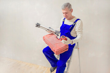 Worker sits on ladder holding laser level for construction and finishing works. © sablinstanislav