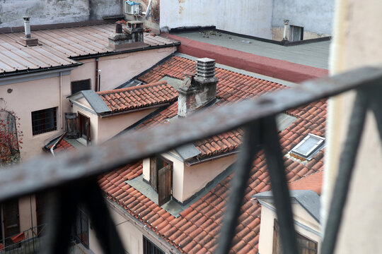 Scorcio panoramico sui tetti in tegole di un palazzo storico veneziano con abbaini e finestre, fotografato attraverso la ringhiera sfocata di un balcone a Venezia