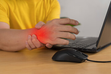 Fototapeta premium Closeup of wrist pain while using computer mouse and laptop at desk