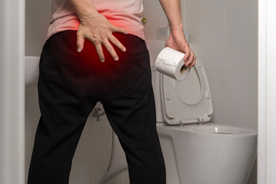 Man with hemorrhoid pain holding toilet paper in bathroom
