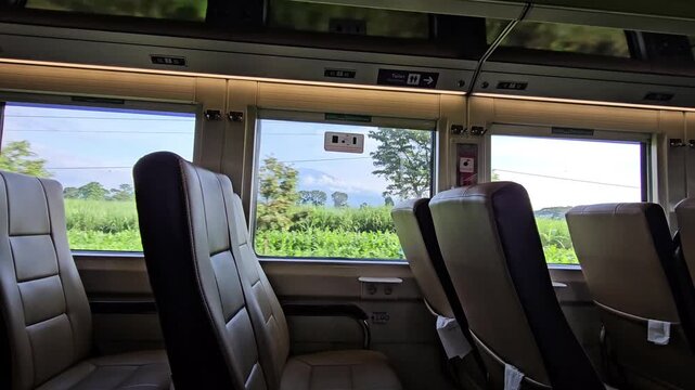 POV video from inside train through window showing mountain silhouette, passing houses, railway motion blur, window frame, and changing outdoor scenery.