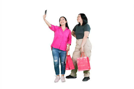 Two Happy Young Asian Women Holding Shopping Bags and Taking a Selfie on White Background