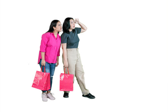 Two Young Asian Women Holding Shopping Bags and Looking Up with Curious Expressions