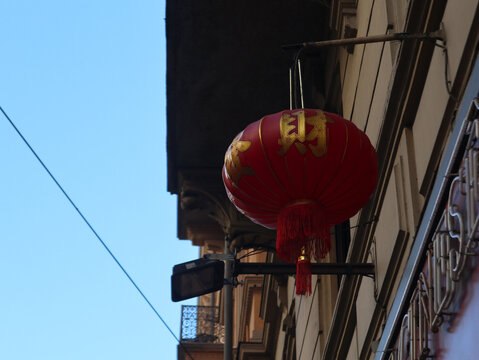 Lanterna cinese rossa tradizionale con ideogrammi dorati appesa all'esterno di un edificio urbano, decorazione asiatica per festivit&agrave; e capodanno sotto un cielo blu limpido