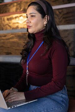 Woman working on silver laptop on tiered seating wearing maroon sweater with blue lanyard and keys