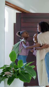 Vertical video: Returning to wooden door, mom opening and guiding child in with mint-green backpack