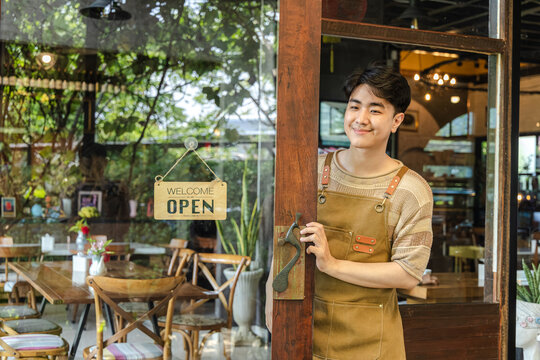 Young barista cafe owner flipping sign to open on storefront door, welcoming customers with confident smile, small business startup energy and positive service mindset in hospitality environment.
