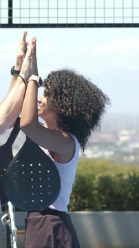 Vertical video: Smiling woman in purple top high-fiving friend coming left on roof, paddle in hand