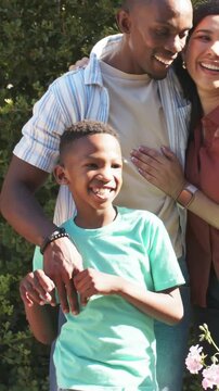 Vertical video: Placing hand on son's shoulder, dad leading trio posing in yard, rust top, pink pot