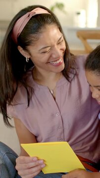 Vertical video: Girl entering right joining mom reading yellow card on sofa with band sharing joy