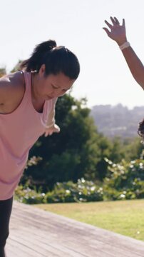 Vertical video: Raising lady in pink warming side-bend on park deck wrist-trackers, copy space