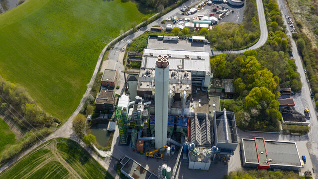 Aerial view of the MVA Hamm waste-to-energy plant with its tall chimney stack and industrial buildings surrounded by green fields in Hamm, Nordrhein-Westfalen, Germany.
