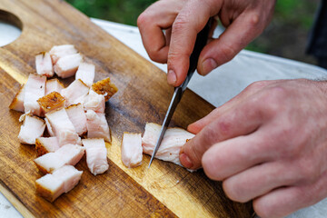 Obraz premium Man's hands slicing salted pork fat into cubes on a wooden cutting board.
