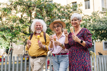 Fototapeta premium Group of happy senior friends eating tasty ice cream cones, smiling and laughing outdoors in an urban setting
