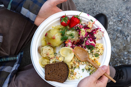 Close-up of picnic meal on disposable plate featuring boiled potatoes beet salad strawberries and dark bread with wooden spoon, selective focus