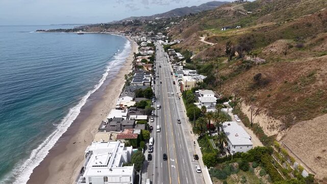 Cinematic 4K 10-bit aerial drone footage captured above the Pacific Coast Highway in Malibu, featuring a smooth reverse dolly while slightly ascending.
