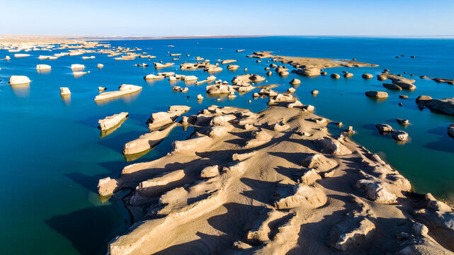 Aerial view of Yadan landforms rising from turquoise water in Dachaidan, Qinghai, China. Unique desert geology forming island-like rock formations in a rare water-covered Yardang (Yadan) landscape.