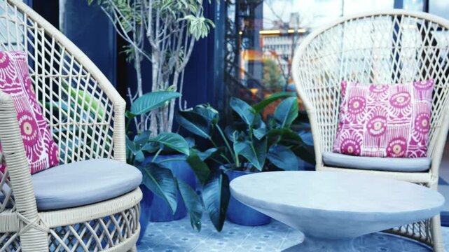 Wide view of an outdoor lounge area featuring woven wicker sofas and decorative pink cushions with circular patterns on a sunny patio.