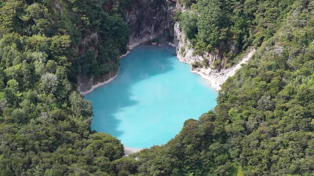 Aerial orbit of bright turquoise volcanic crater lake in Waimangu Volcanic Valley, New Zealand, drone view of scenic geology nature.