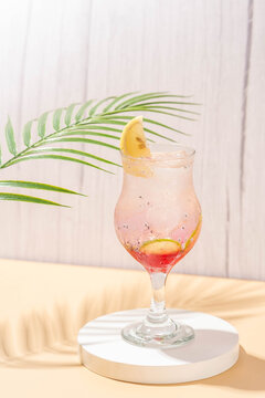 sparkling wardah non alcoholic drink served in a glass on a cream colored table with a white stone coaster, a wooden patterned background, and leaves palm as decoration.