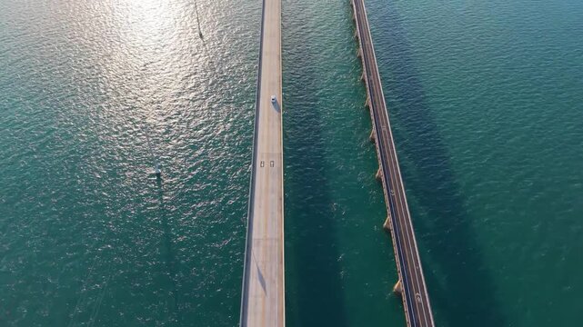 Cinematic aerial drone shot capturing the parallel span of the modern Overseas Highway and the historic Old Seven Mile Bridge over emerald waters.