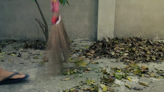 Man sweeping dry fallen leaves with traditional coconut leaf ekel broom on concrete yard outdoors