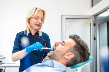 Fototapeta premium Female physician performing tooth extraction for male patient with dental pliers. Blonde woman doctor conducting oral surgery in modern clinic. Healthcare and medicine professional dental service.